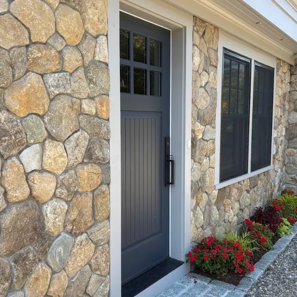 Custom fieldstone veneer on a home entry with a gray door and red flower bed