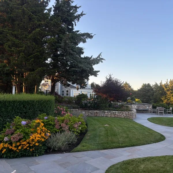 Landscape design with a bluestone walkway, fieldstone wall, lawn, and flower beds at a Cape Cod home